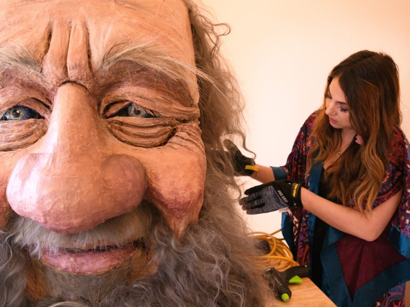 A woman paints the beard of a giant puppet head