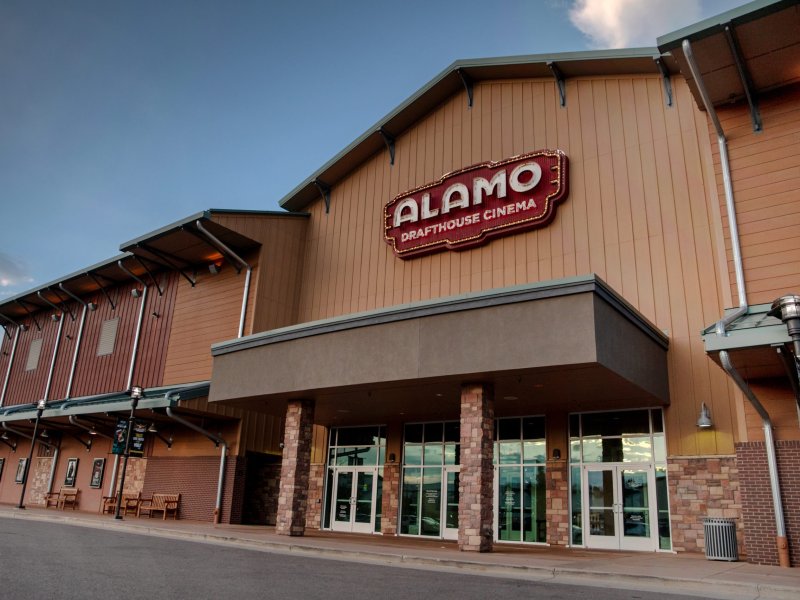 Exterior view of the Alamo Drafthouse Cinema with a prominent sign above the entrance, showing a modern building design with a clear sky backdrop.