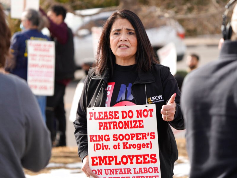 A woman wearing a sign supporting a strike talks to the press