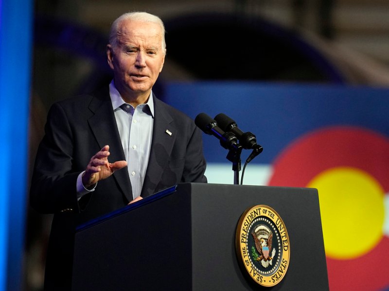 Joe Biden in a suit speaks into microphones on a podium with a presidential seal.