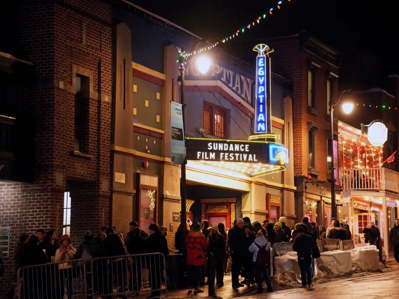 A crowd gathered outside the historic Egyptian Theatre at night for the Sundance Film Festival, with festive lights illuminating the street.