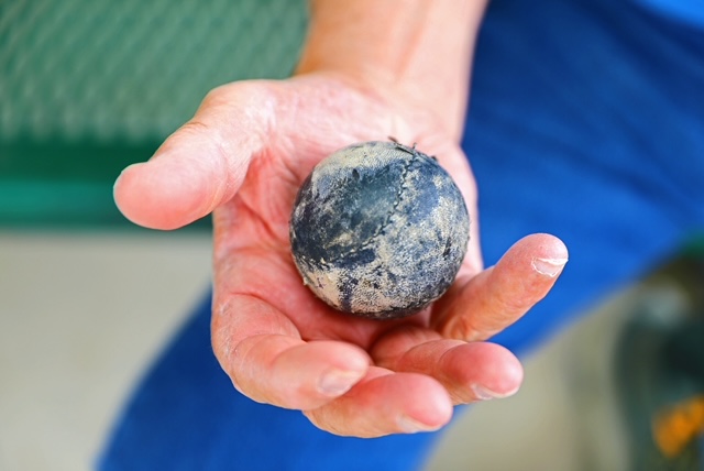 A person holding a worn, blackened ball in their hand.