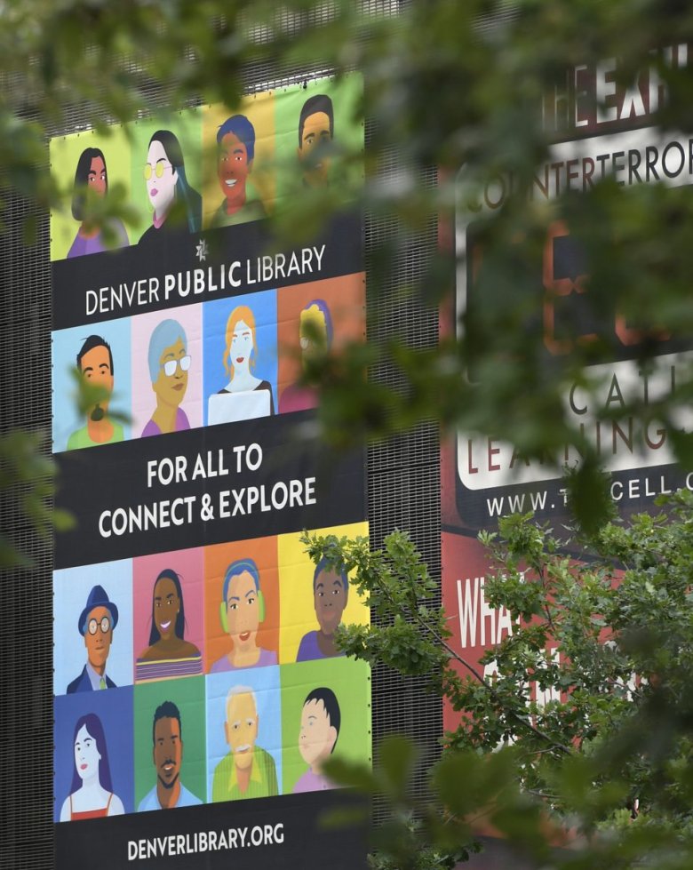 A banner promoting the Denver Public Library with illustrations of diverse people and text that reads "For All to Connect & Explore" partially obscured by tree branches.