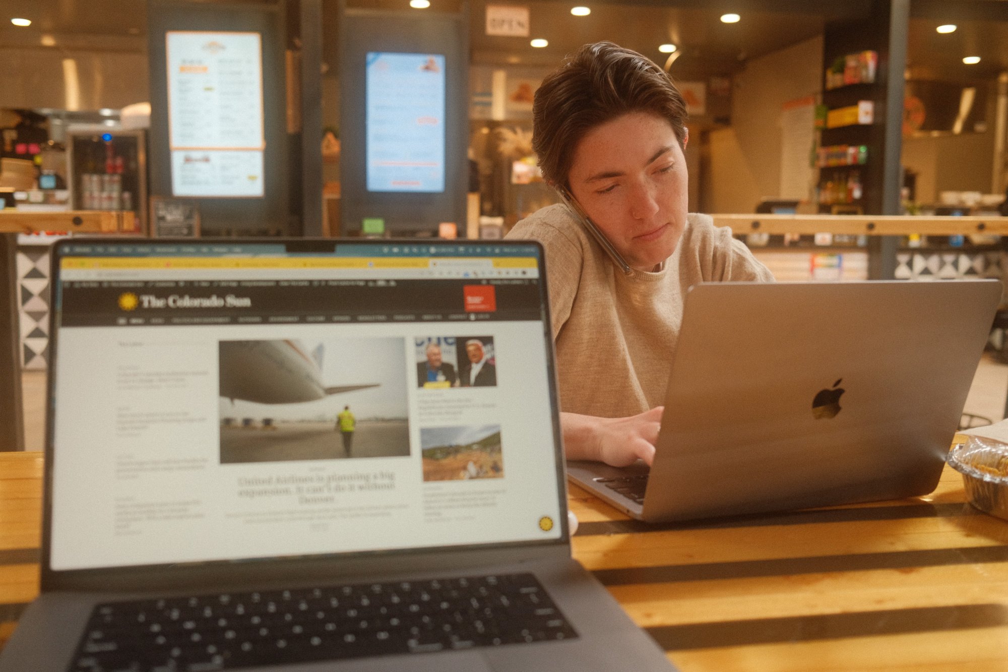 A woman holds a phone to her ear using her shoulder while typing on a laptop.