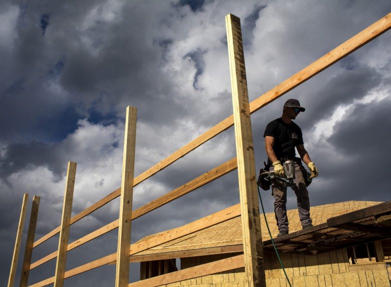 A construction worker stands atop a roof while working on a house.