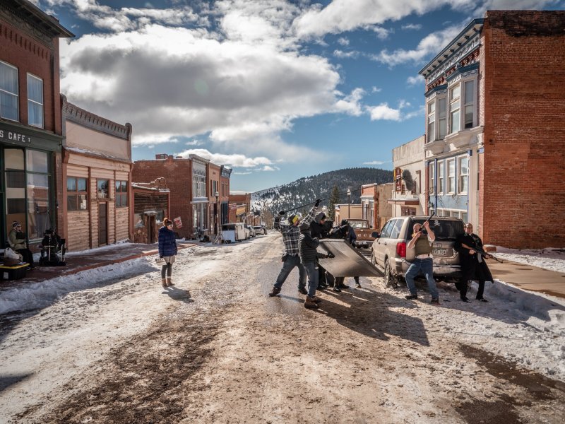 A crew films two actors dressed as law enforcement in a small town with snow on the ground.