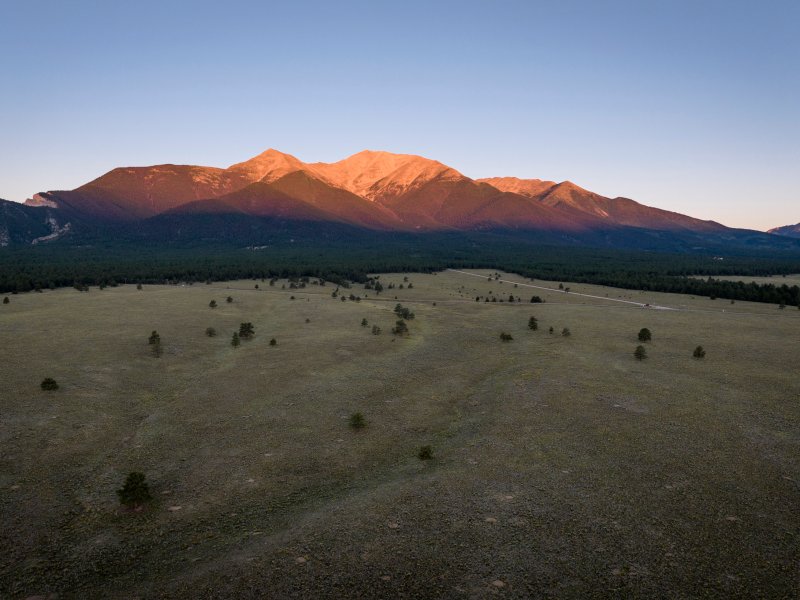 A tall mountain highlighted by an orange sunrise light above the valley in the shadow