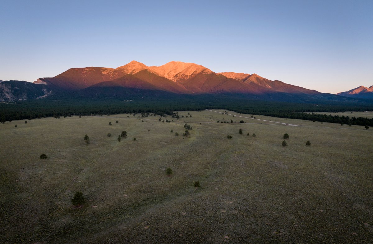 A tall mountain highlighted by an orange sunrise light above the valley in the shadow