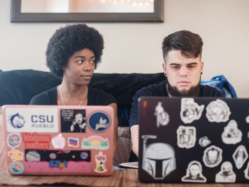 A woman on her laptop looks over to a boy working on his laptop next to her