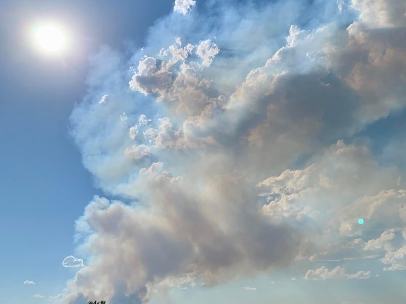 Smoke billows from mountains in the distance, beyond a lake and a sign reading road closed