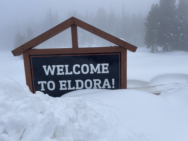 snow falling on drifts against a sign that says Welcome to Eldora