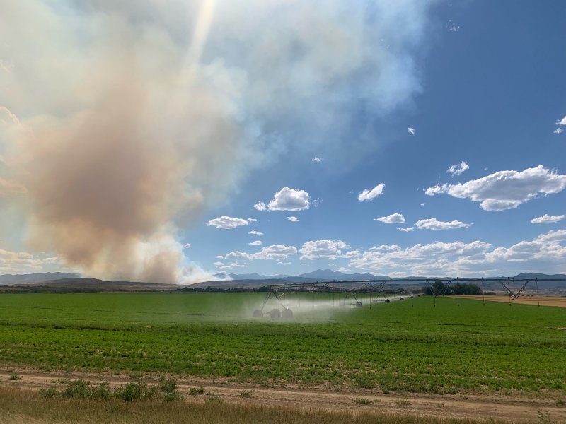 A huge plume of smoke visible on the horizon with crops being irrigated in the foreground.