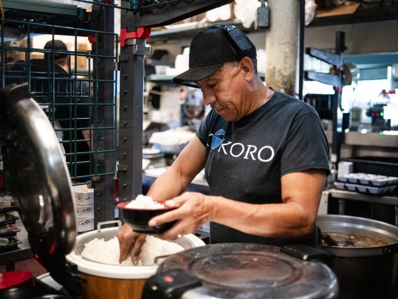 A man scoops rice into a bowl while working in a kitchen.