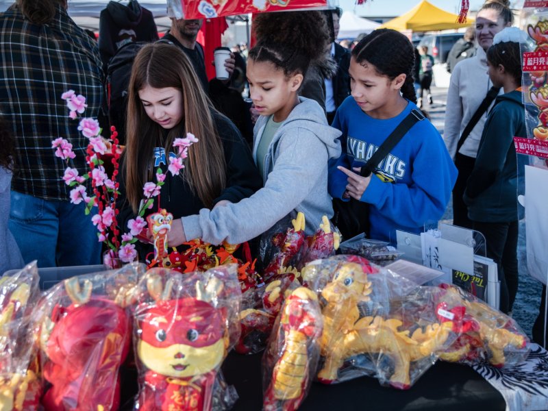 Three young girls look through items on a table at a festival