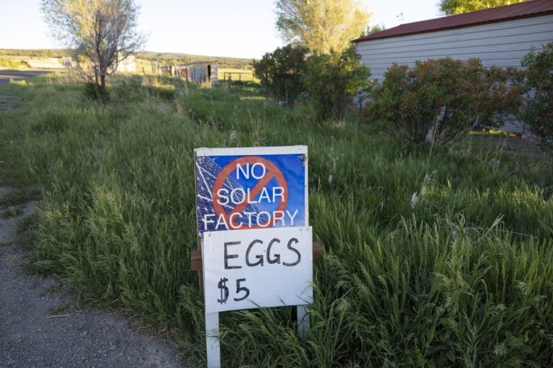 a sign saying "no solar factory" sits above a sign saying "eggs $5" on the ground outside