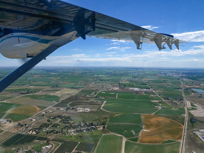 View from an airplane showing agricultural fields and rural landscape under a clear blue sky.