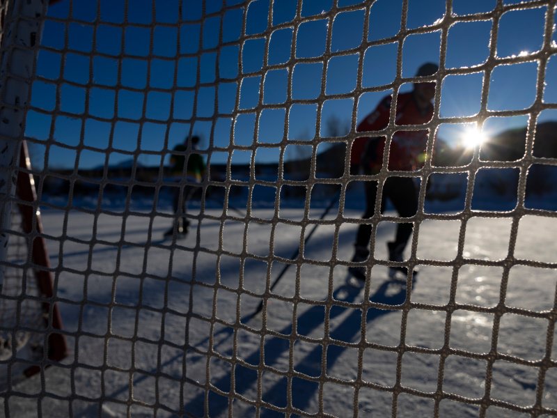 A goalie net facing the sunlight with two hockey players out of focus in background