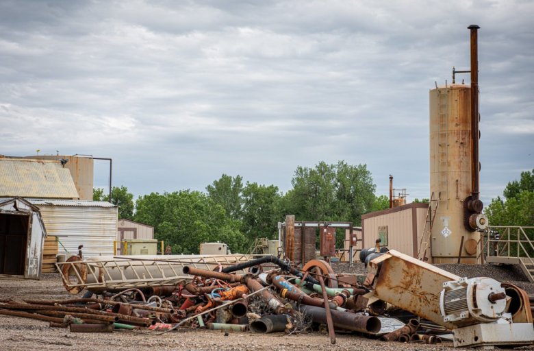 A photo of piles of scrap metal, pipes and and a dehydrator on the ground near equipment used to separate hydrocarbons from water after being pumped from the ground.