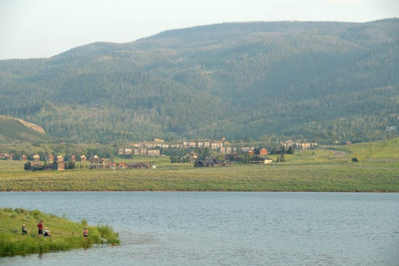 A family and dog play in a large reservoir in the foreground. Behind them are houses on the other side of the water.