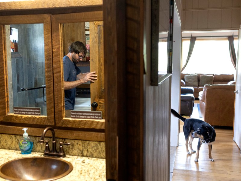 A man does laundry in a bathroom with his dog in hallway.