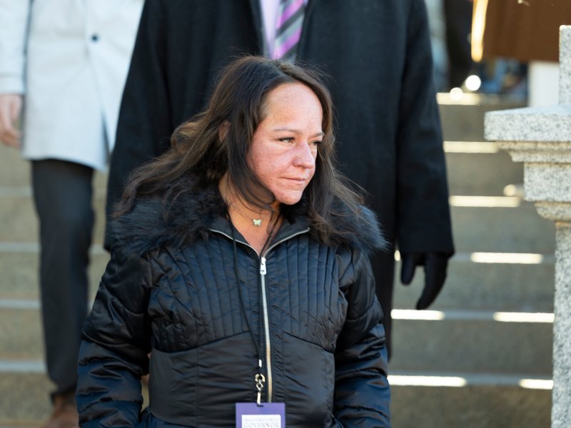 Faith Winters, with long brown hair wearing a black jacket and a badge on a lanyard, walks down outdoor steps.