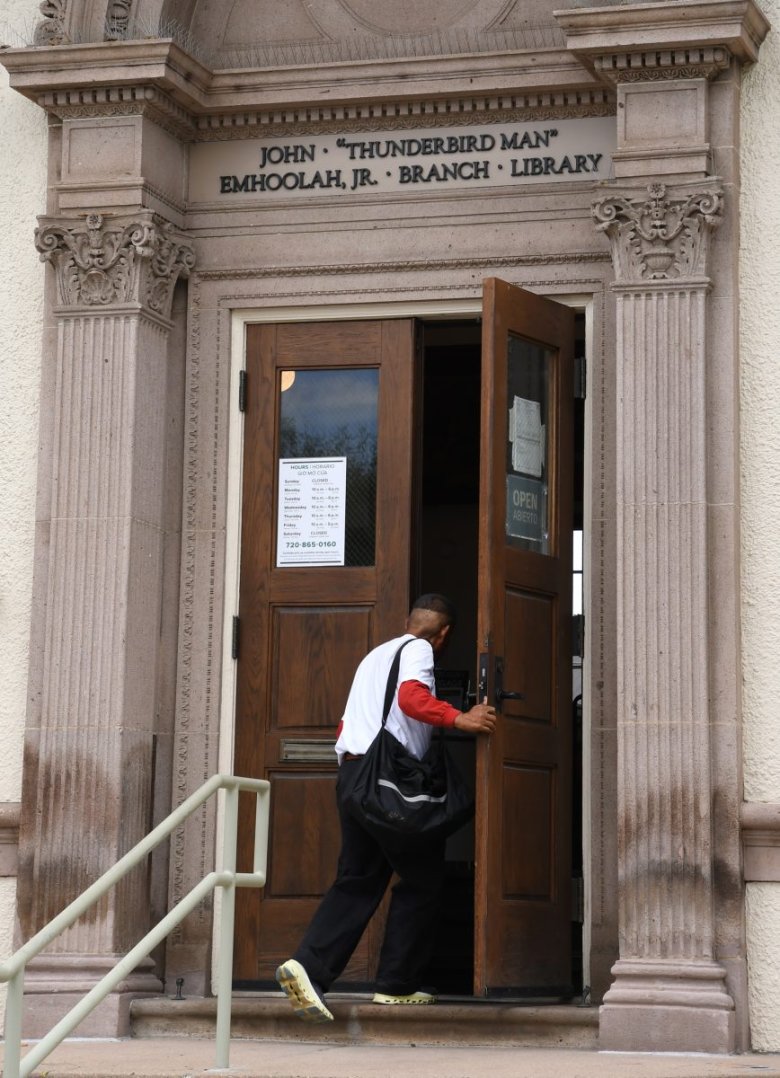 A person with a black bag walks into the John "Thunderbird Man" Emhoolah Jr. Branch Library through a door marked open.