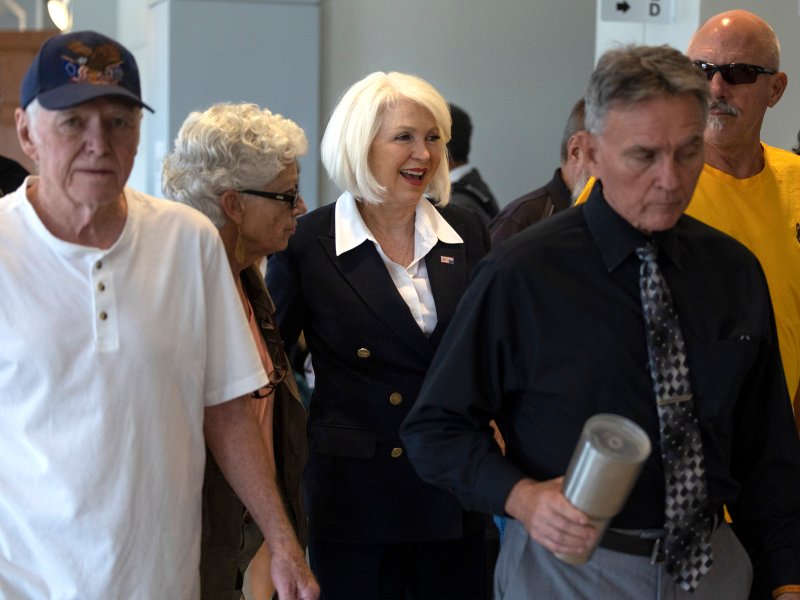 People inside a building with Tina Peters, who has light color short hair, in the middle.