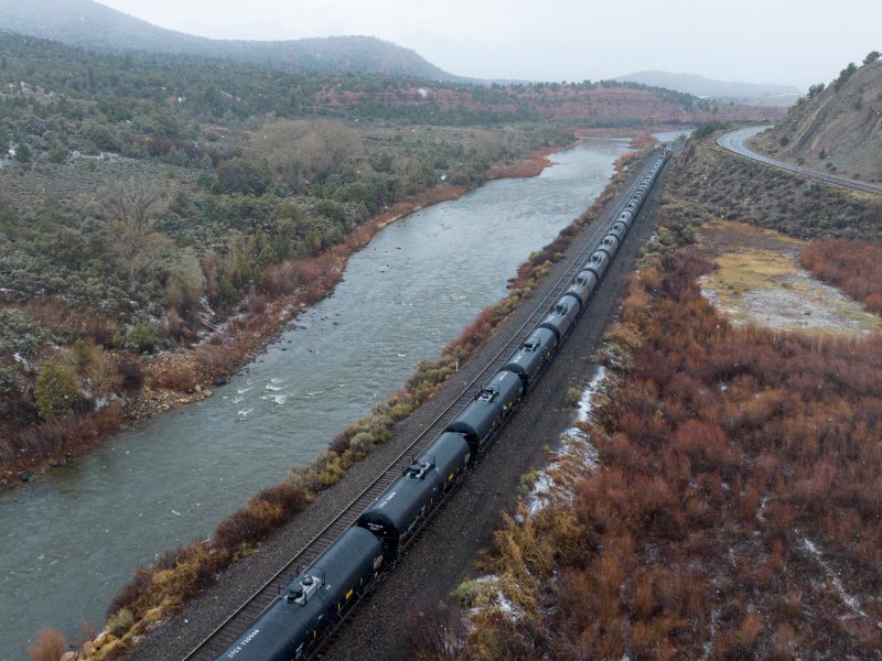 aerial view of train tracks with dark cylinder shape train cars next to a river