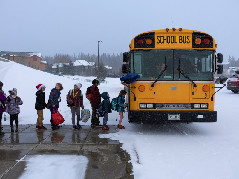 A line of kids getting onto a bus as snow covers the ground