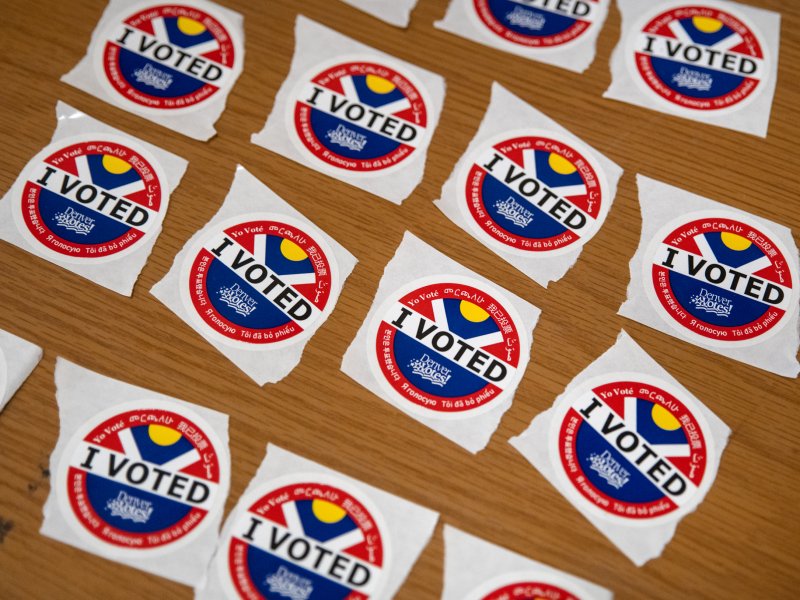 A table is covered with multiple "I Voted" stickers featuring a flag design with red, white, blue, and yellow colors.